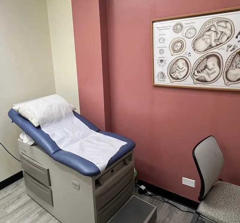 Women's health examination room with examination table and pregnancy development chart at Todu Guam Foundation